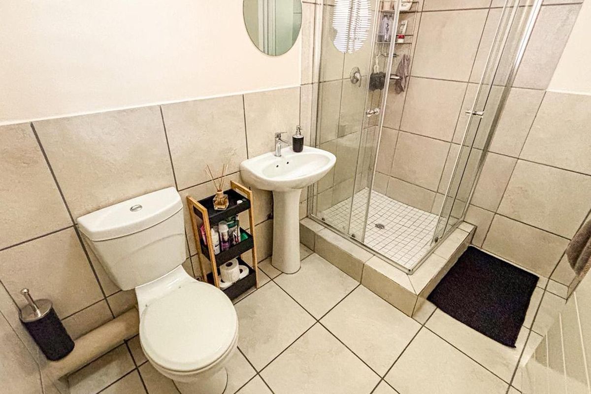 A functional bathroom featuring a pedestal sink, a glass-enclosed shower, and neutral wall and floor tiling.
