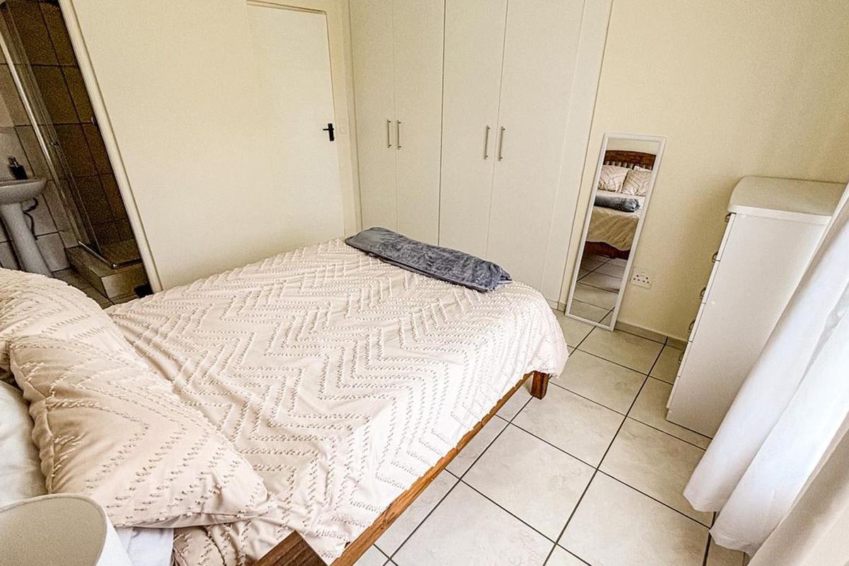 A functional bedroom featuring built-in cupboards, tiled flooring, and direct access to an en-suite bathroom.