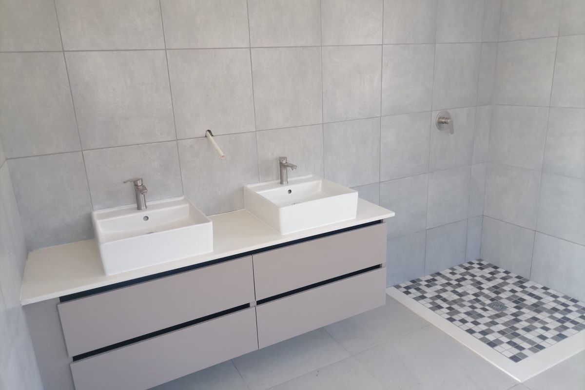 Modern bathroom featuring a double vanity with vessel sinks, grey cabinetry, and a walk-in shower with mosaic tile flooring.