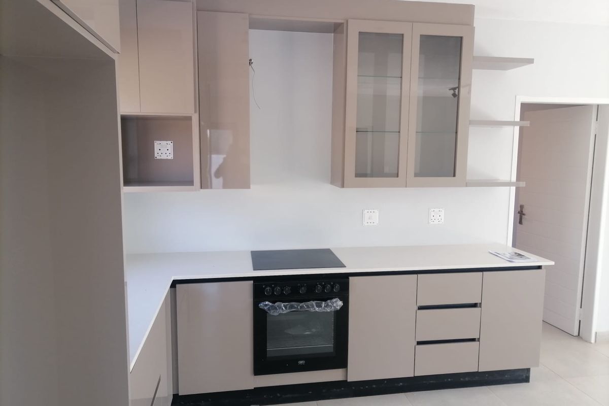 Modern kitchen featuring sleek taupe cabinetry, white stone countertops, a built-in electric oven, and a glass-top hob.