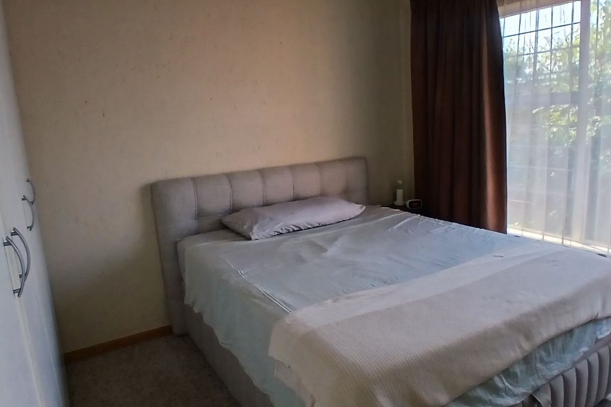 A bedroom featuring built-in cupboards and a large window with curtain tracks, providing natural light.