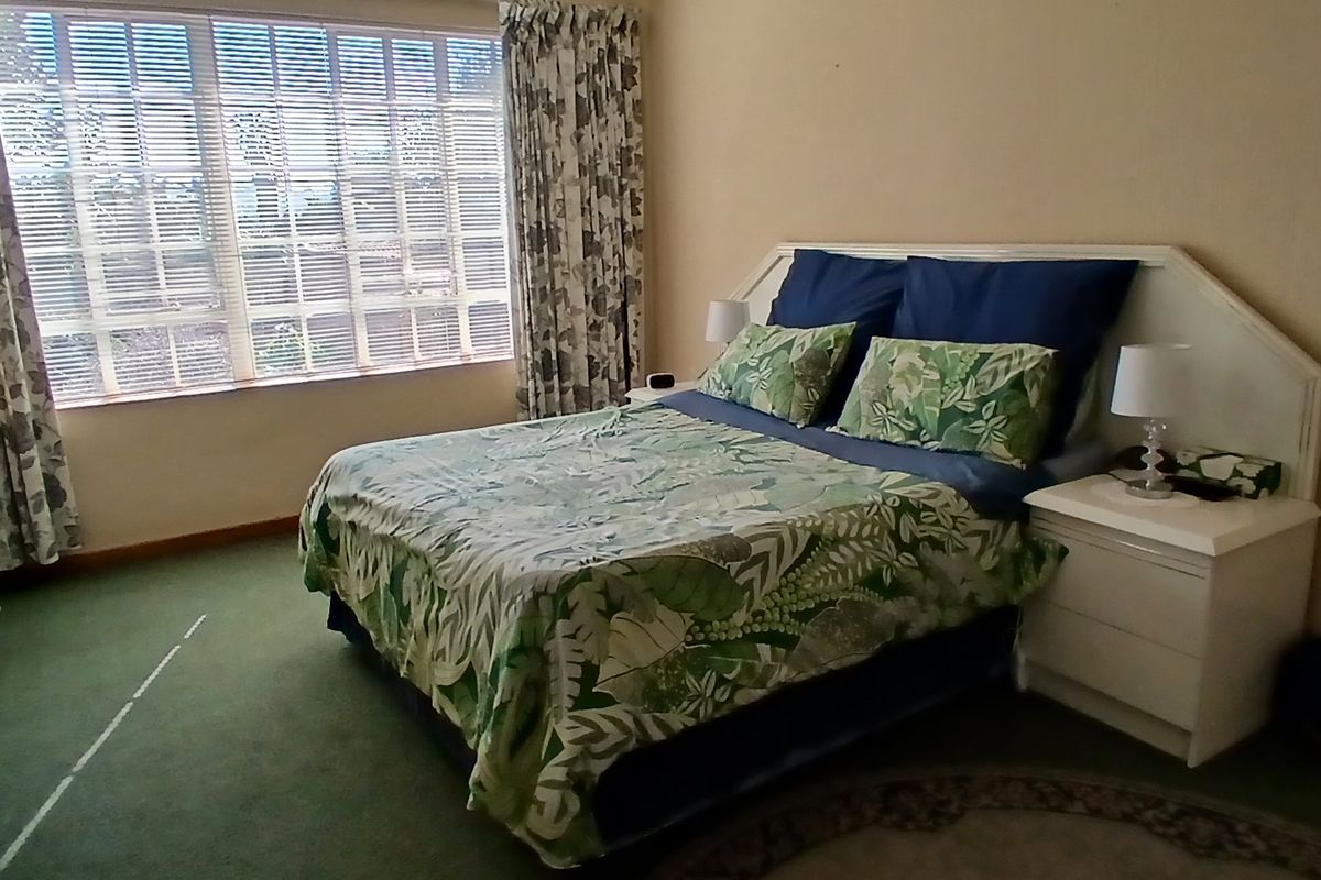 A spacious bedroom featuring large windows with natural light, carpeted flooring, and a built-in headboard structure.