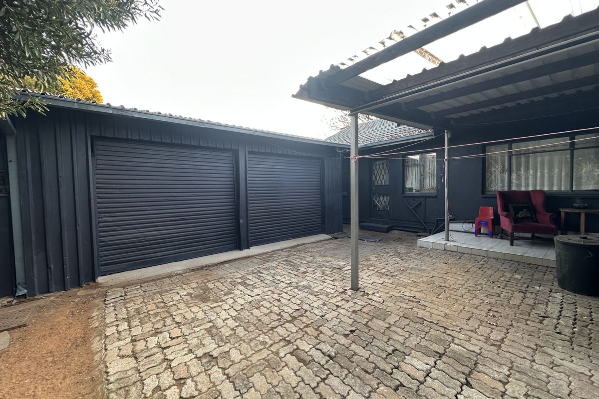 Rear exterior area featuring a double garage with roller shutter doors, a covered patio space, and cobblestone paving.