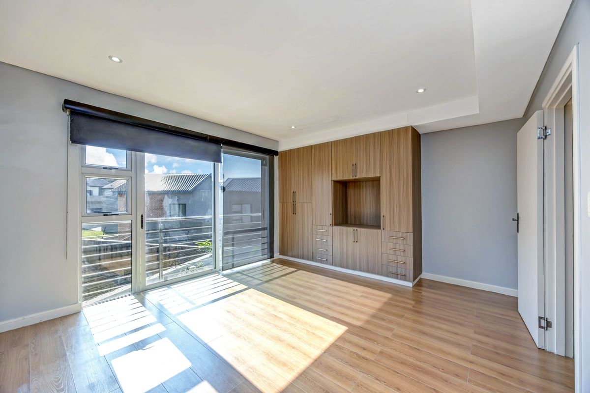 A bright bedroom featuring wood-look tile flooring, built-in cabinetry, and large sliding glass doors leading to a balcony.
