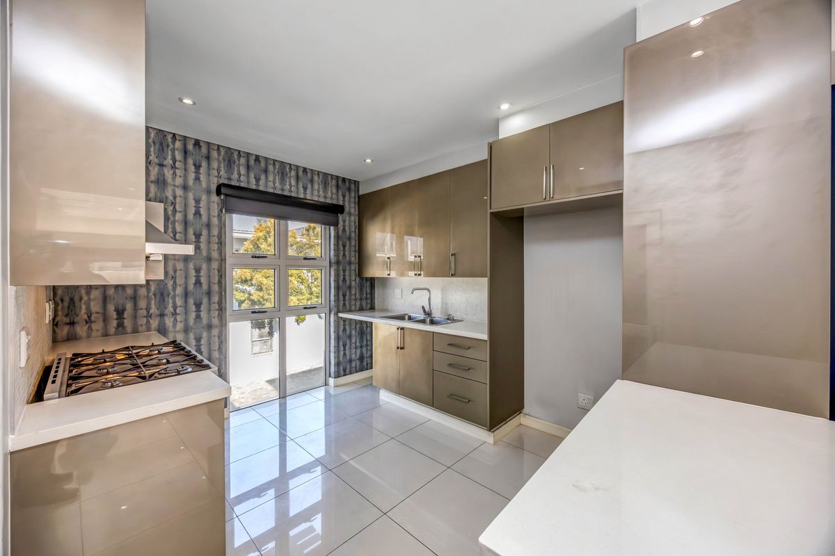 Modern kitchen featuring high-gloss cabinetry, stone countertops, a built-in gas hob, and tiled flooring with a window providing natural light.