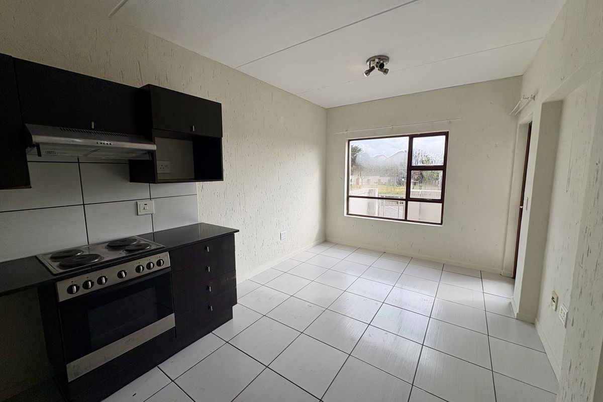 A functional, empty kitchen featuring dark built-in cabinetry, an electric stove with extractor fan, tiled flooring, and a large window providing natural light.