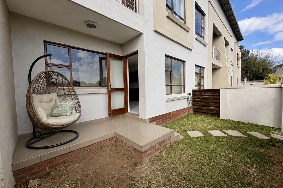 Rear exterior view of the townhouse featuring a tiled patio area, small private garden with stepping stones, and access to the interior living space.