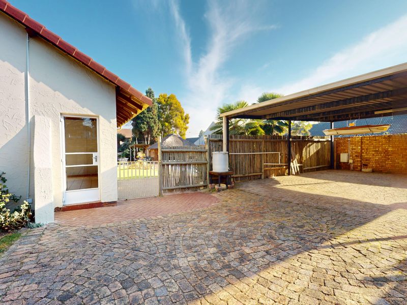 A spacious outdoor area featuring a paved driveway and a covered carport structure with brick and timber fencing.