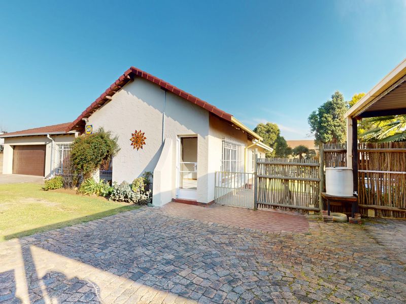 Front exterior view of the house featuring a paved driveway, attached garage, carport, and secure gated entrance with established garden area.