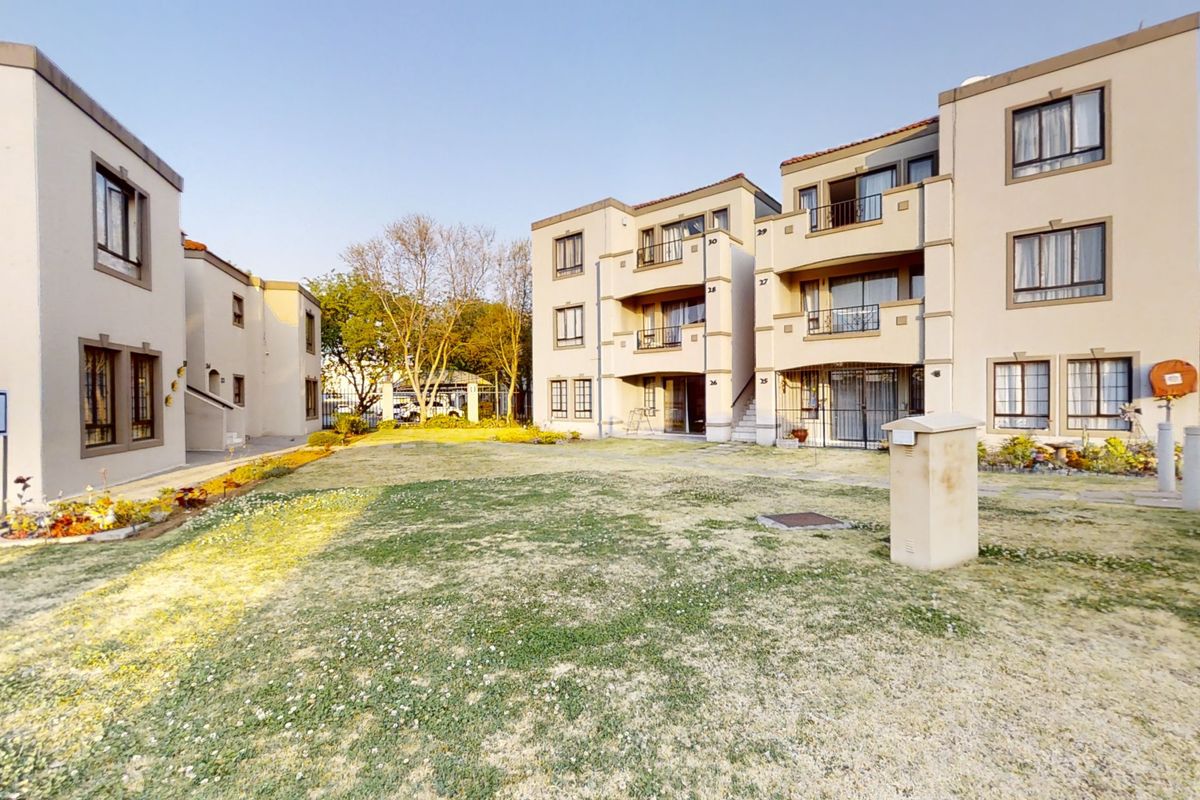 Exterior view of a townhouse complex featuring multi-story residential units, shared garden space, and paved walkways.