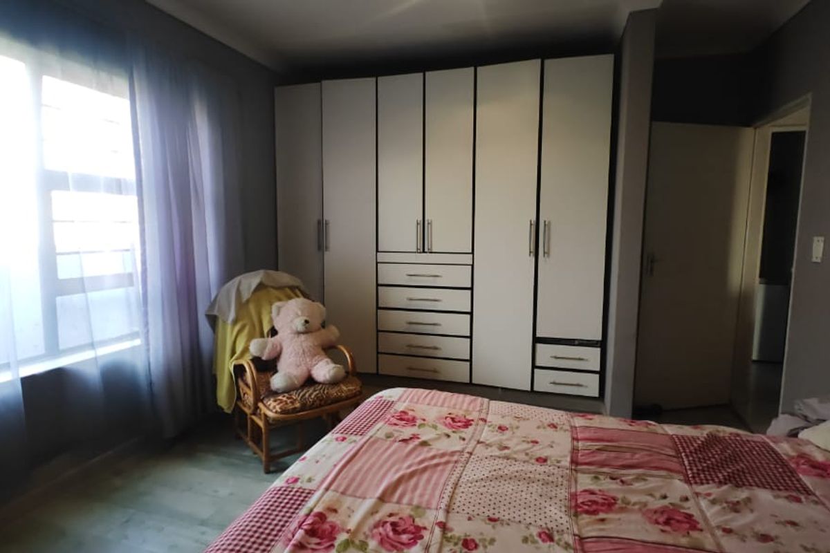 A well-lit bedroom featuring neutral grey walls, laminate flooring, and extensive white built-in cabinetry providing ample storage space.