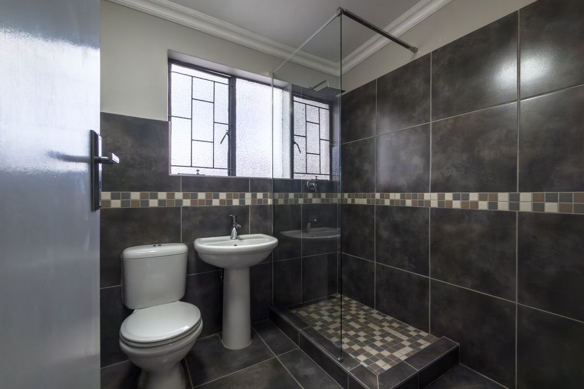 Modern bathroom featuring a walk-in shower with glass enclosure, pedestal basin, and toilet, finished with dark wall and floor tiling.