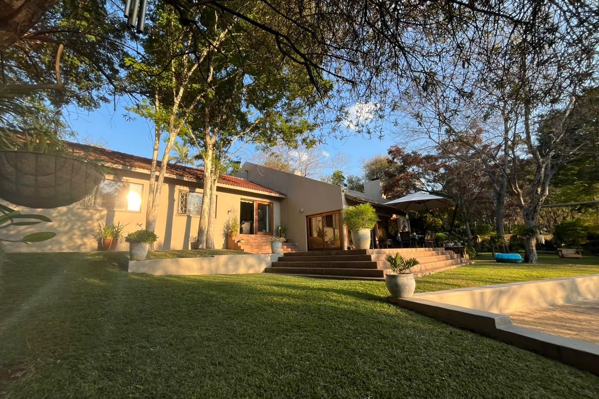 A spacious rear exterior view featuring a landscaped garden, a tiled patio with steps, and a swimming pool set against the house facade.