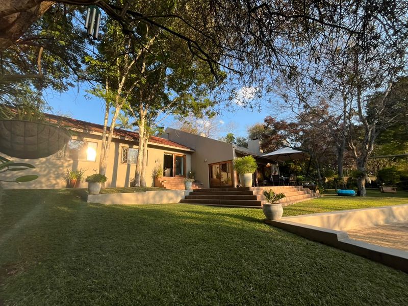A spacious rear exterior view featuring a landscaped garden, a tiled patio with steps, and a swimming pool set against the house facade.