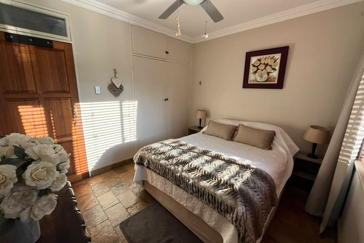 A cozy bedroom featuring stone tile flooring, built-in cupboards, and a ceiling fan, offering a warm and functional living space.