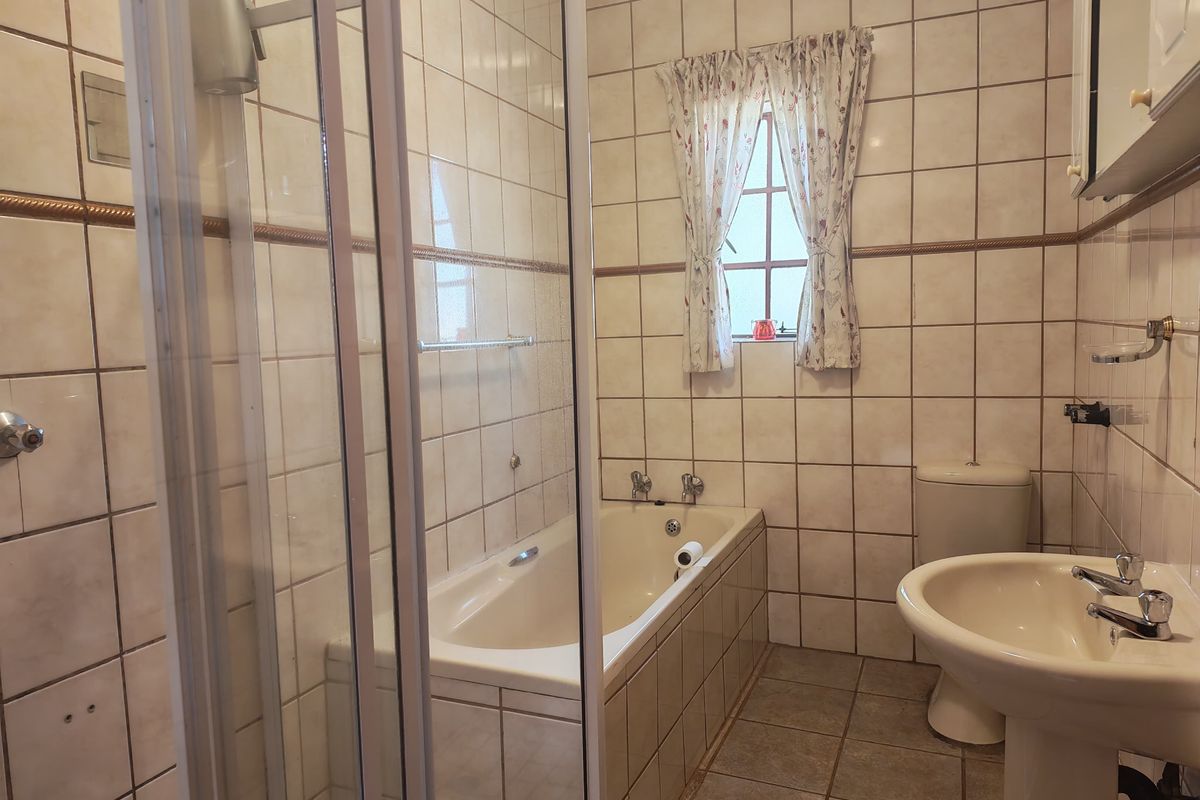 A dated bathroom featuring a shower enclosure, built-in bathtub, pedestal basin, and toilet, finished with neutral ceramic wall and floor tiles.