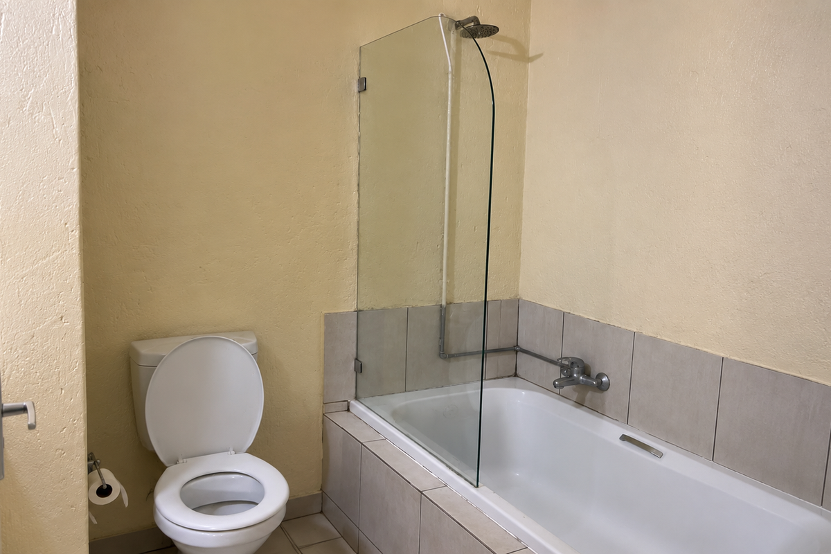 A functional bathroom featuring a bathtub with a glass shower screen, tiled splashback, and a standard toilet.