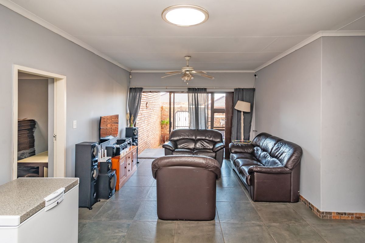 A spacious living room featuring tiled flooring, a ceiling fan, and a sliding glass door providing access to the rear patio area.