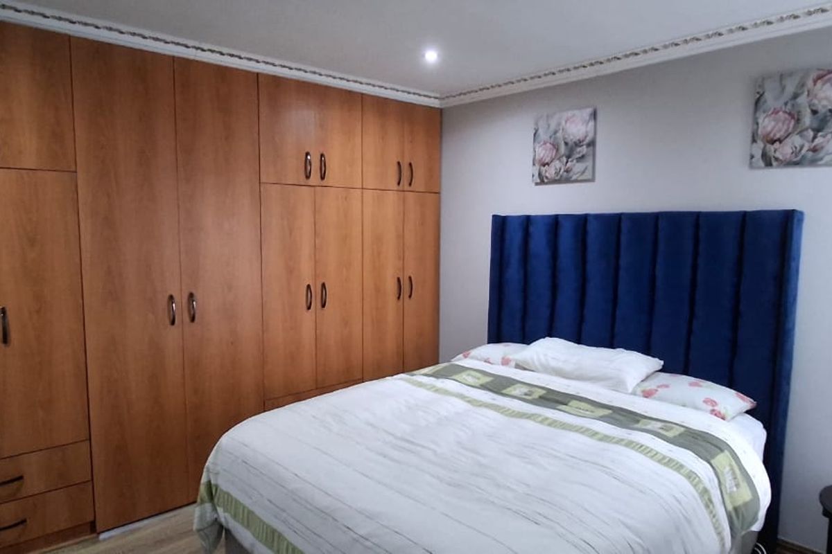 A well-maintained bedroom featuring extensive floor-to-ceiling built-in wooden cupboards, laminate flooring, and decorative crown molding.