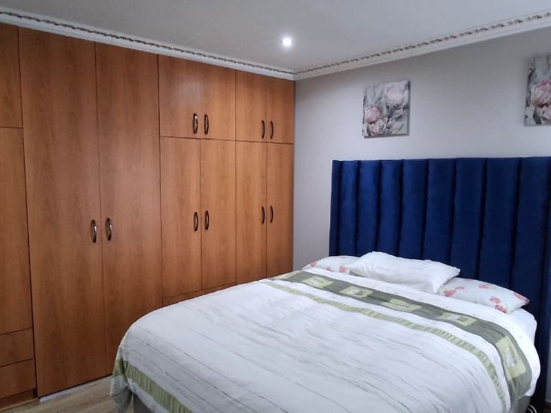 A well-maintained bedroom featuring extensive floor-to-ceiling built-in wooden cupboards, laminate flooring, and decorative crown molding.