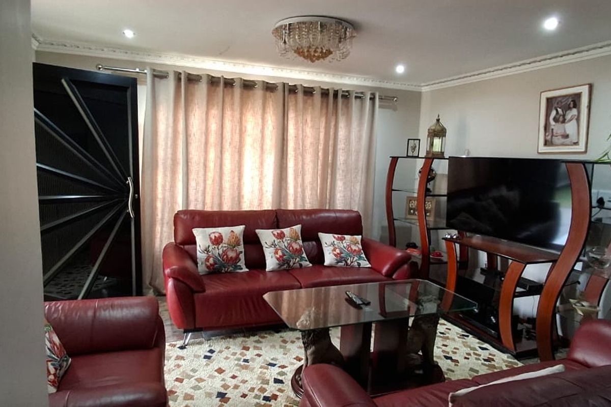A well-maintained living room featuring decorative ceiling cornices, recessed downlighting, a central crystal chandelier, and a modern security entrance door.