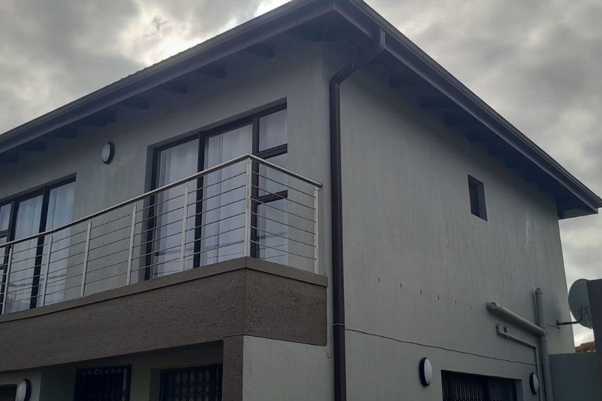 A view of the rear exterior facade featuring a balcony with a stainless steel balustrade and modern sliding doors.