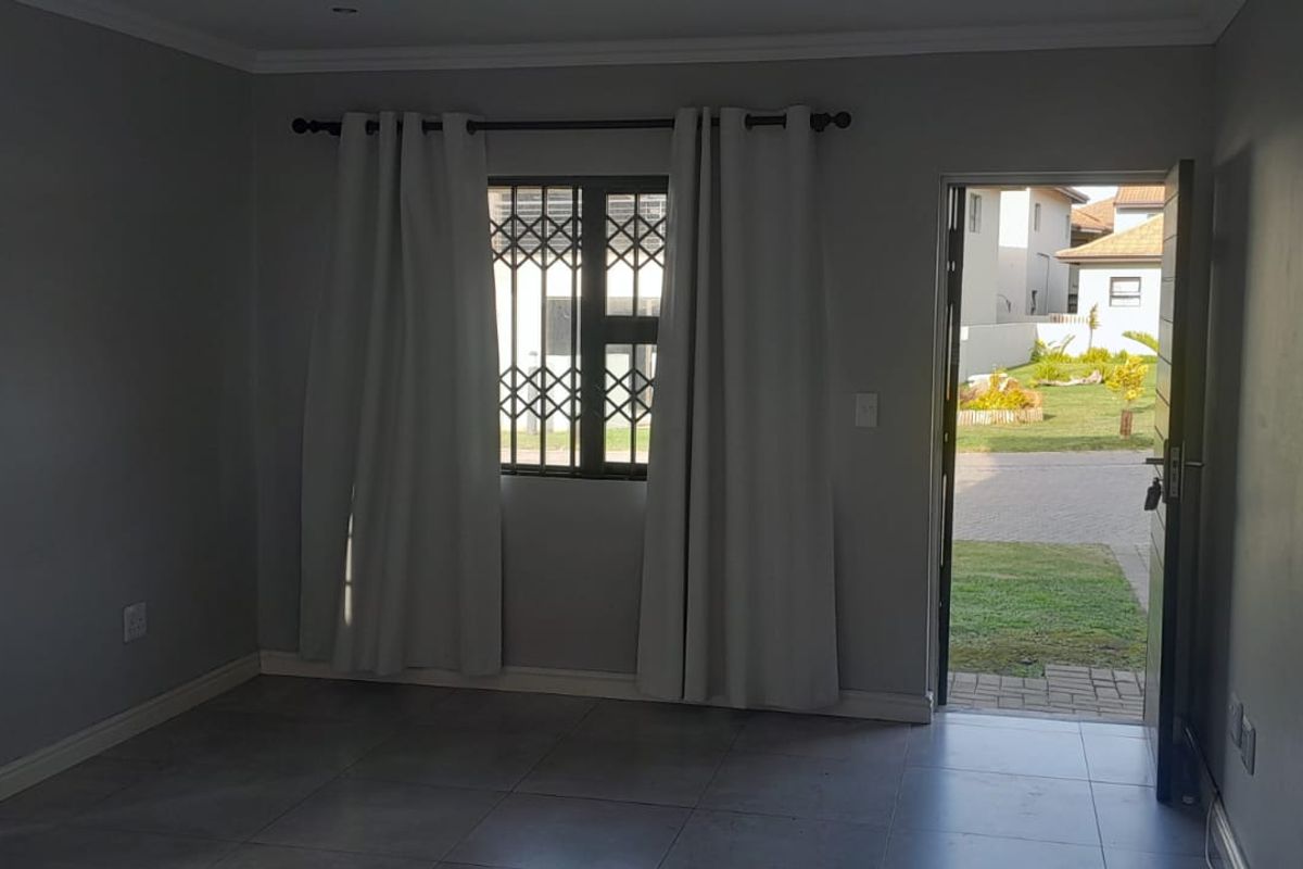 An empty living room featuring neutral tiled flooring, security bars on the window, and direct access to the exterior garden area.