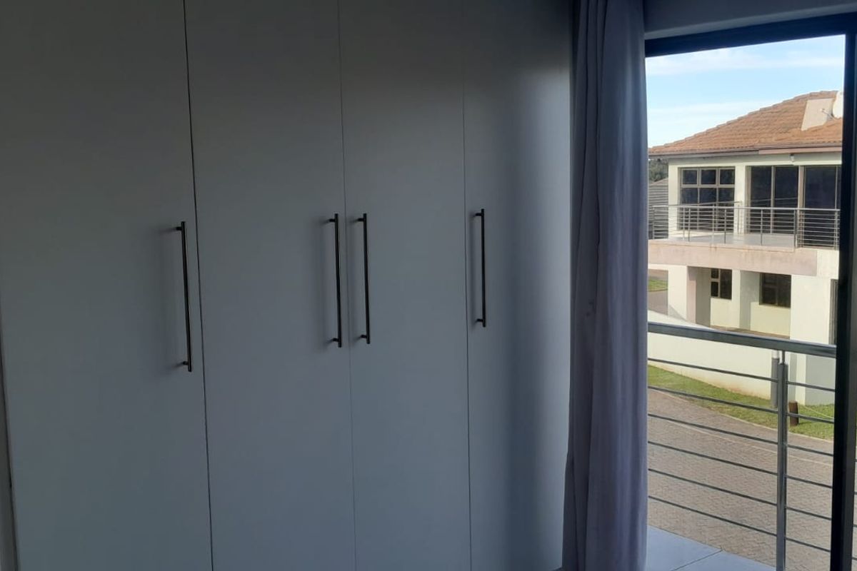 A bright bedroom featuring modern built-in cupboards and a sliding glass door that opens onto a balcony with neighborhood views.