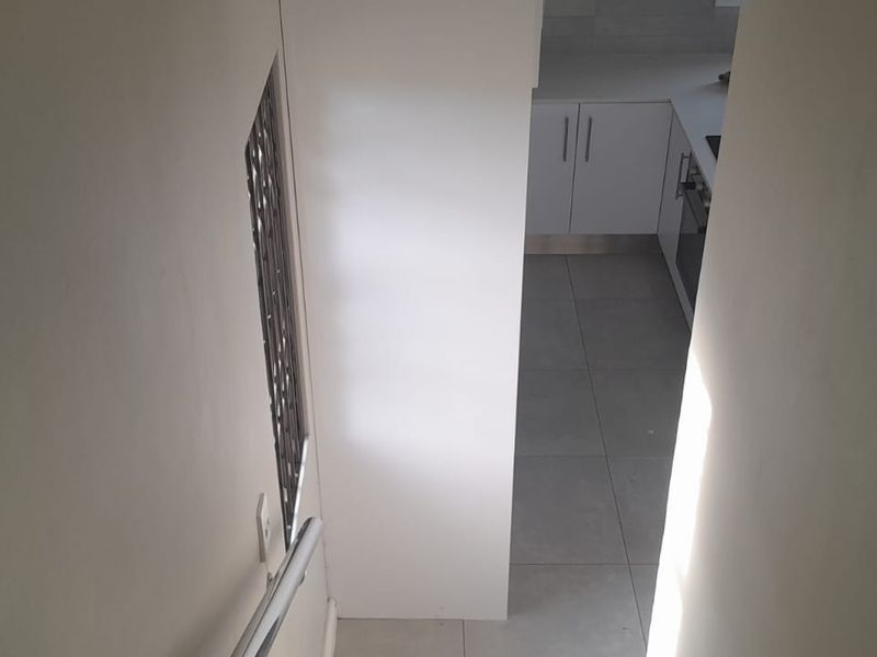A view looking down a staircase towards a modern kitchen area featuring white cabinetry and tiled flooring.