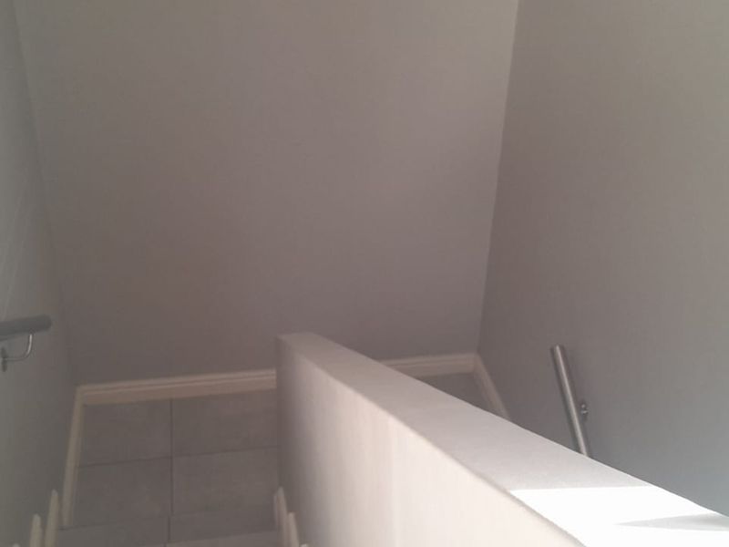 A clean and minimalist staircase area featuring neutral grey walls, tiled flooring, and a modern handrail.