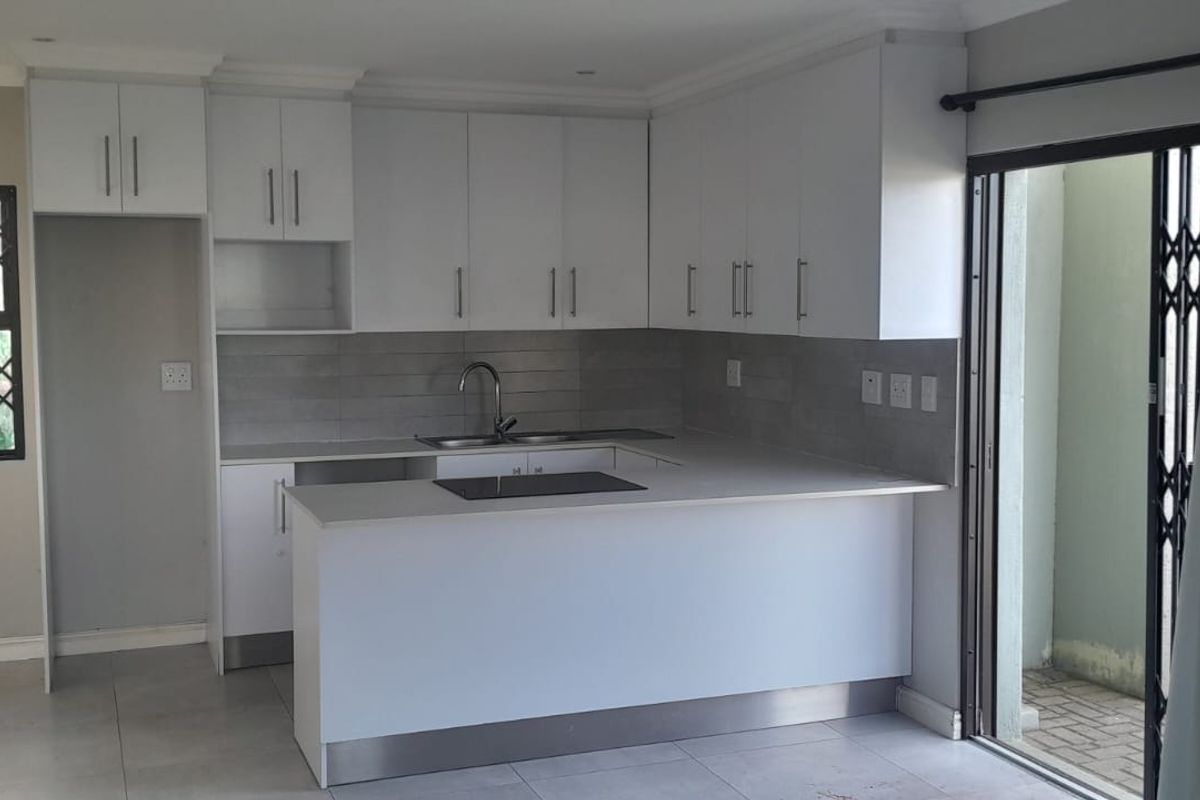 Modern kitchen featuring white cabinetry, stone countertops, integrated hob, and tiled splashback, with direct access to an outdoor area through a sliding door.