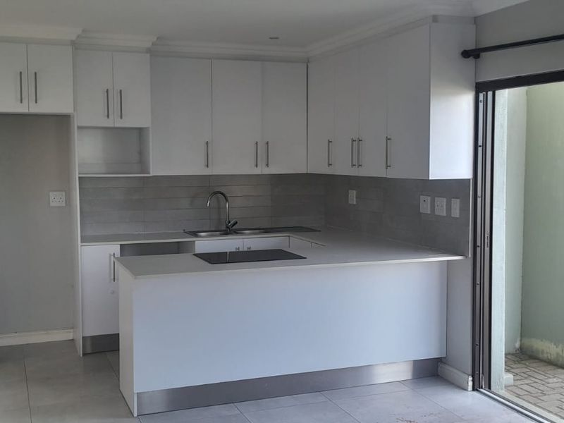 Modern kitchen featuring white cabinetry, stone countertops, integrated hob, and tiled splashback, with direct access to an outdoor area through a sliding door.