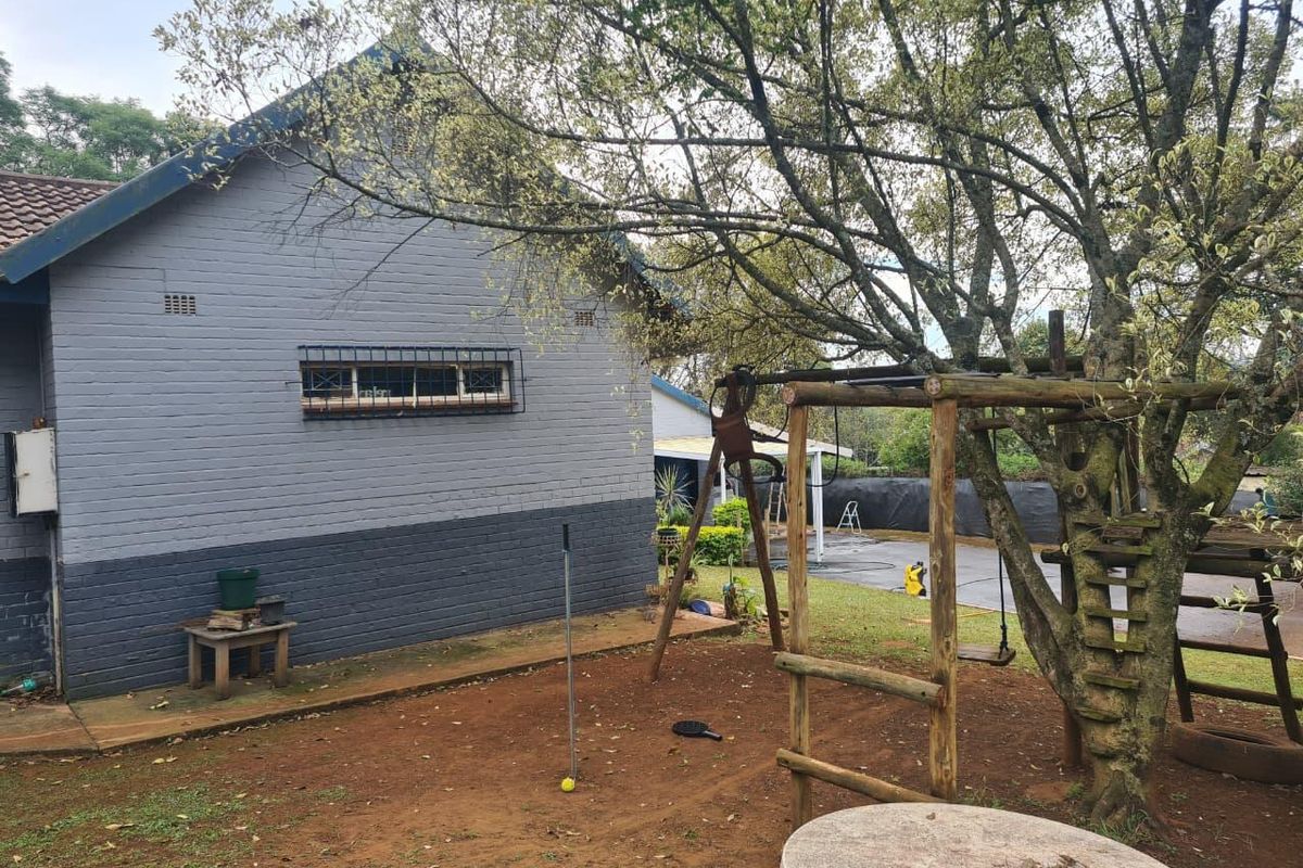 Rear view of the property featuring a painted brick facade, security window bars, and a garden area with paved sections.