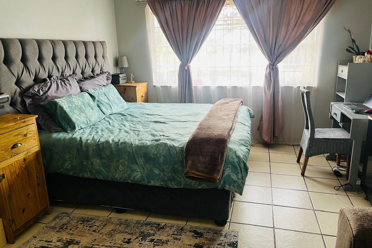 A functional bedroom featuring tiled flooring and a window fitted with security bars, providing natural light and essential security.