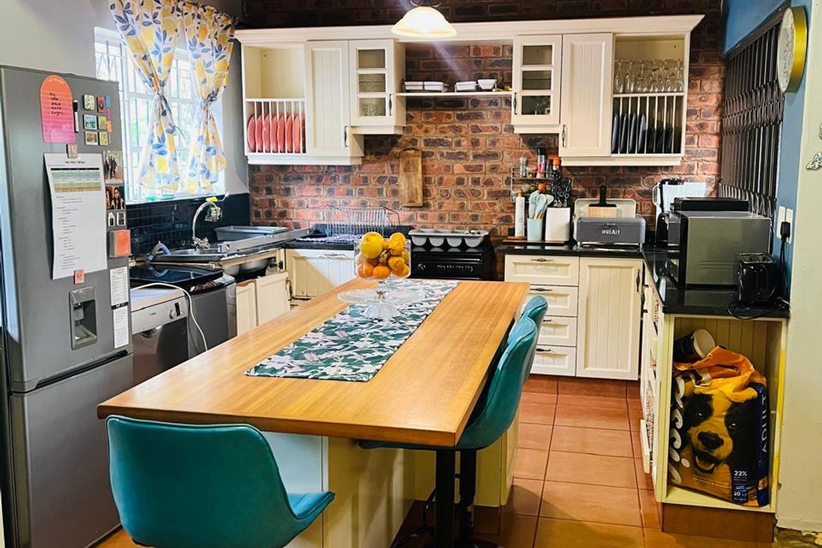A kitchen featuring an exposed brick wall, timber ceiling, tiled flooring, and a central island with built-in cabinetry and a double sink.