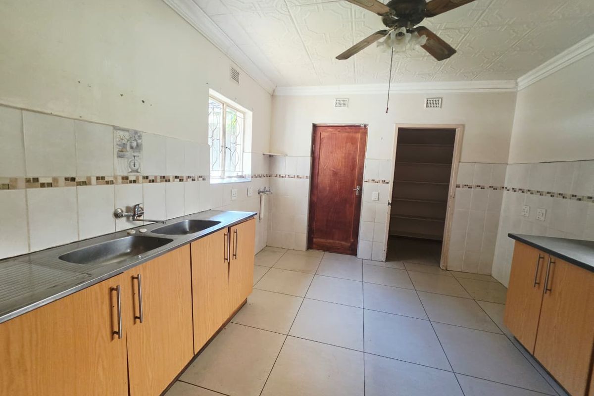 A functional kitchen featuring laminate cabinetry, double stainless steel sink, tiled splashbacks, and an adjoining walk-in pantry, ready for modern updates.