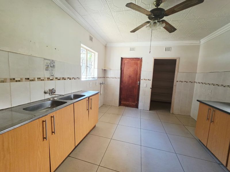 A functional kitchen featuring laminate cabinetry, double stainless steel sink, tiled splashbacks, and an adjoining walk-in pantry, ready for modern updates.