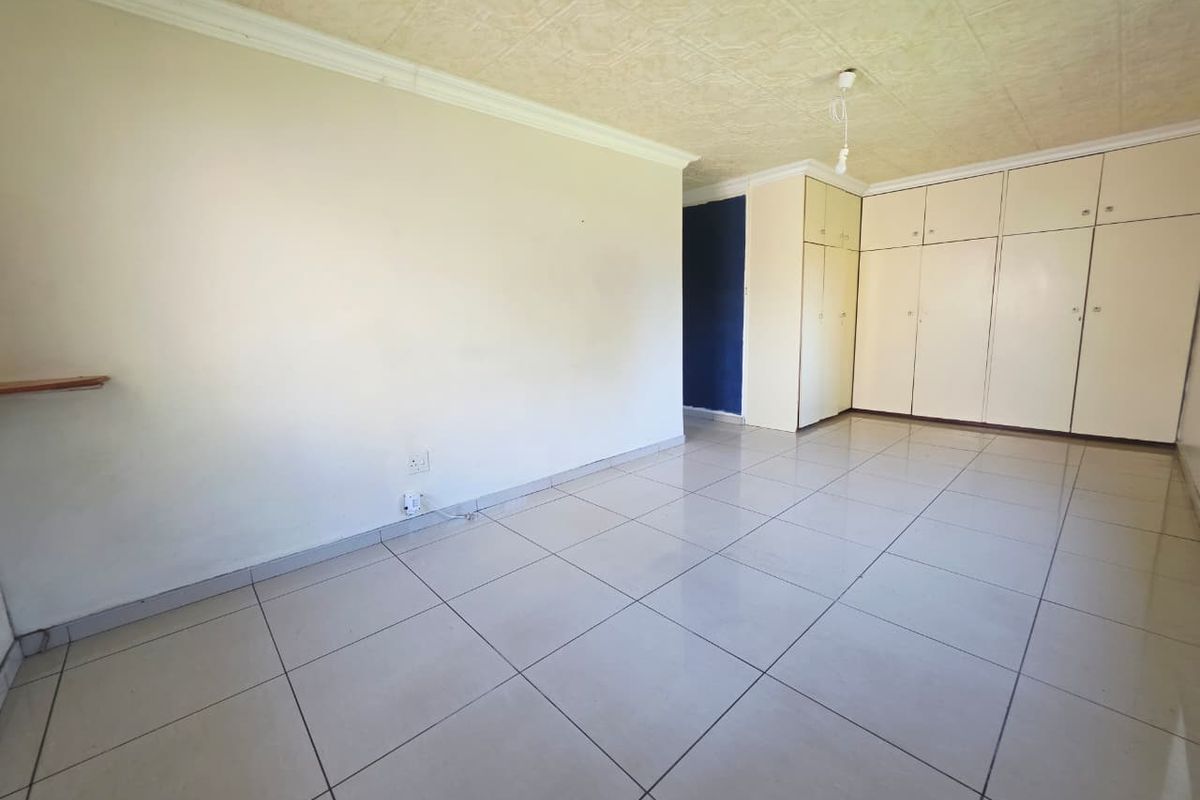 A spacious, empty bedroom featuring neutral tiled flooring, built-in storage cupboards, and textured ceiling tiles.