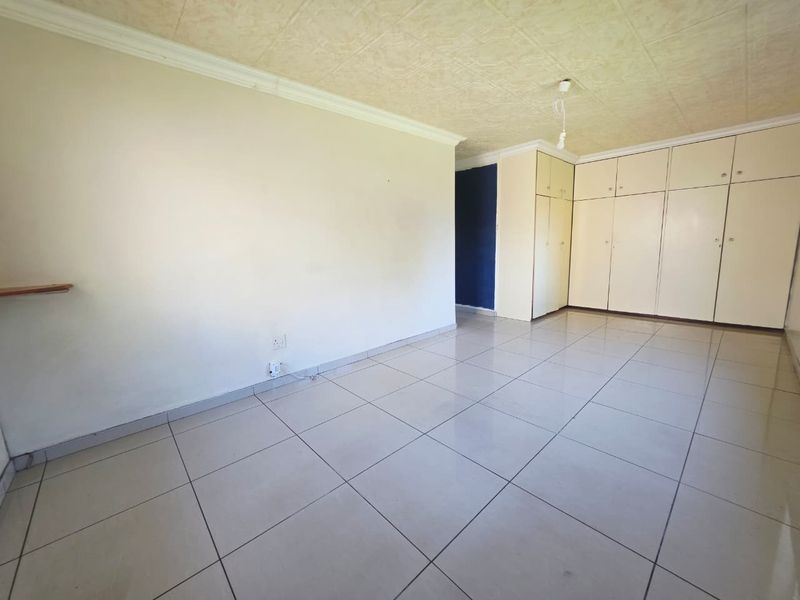 A spacious, empty bedroom featuring neutral tiled flooring, built-in storage cupboards, and textured ceiling tiles.