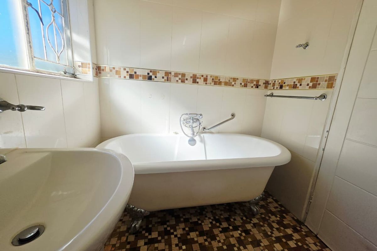 A dated bathroom featuring a classic clawfoot bathtub, pedestal basin, and mosaic tile flooring with decorative wall accents.