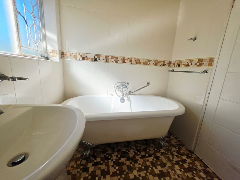 A dated bathroom featuring a classic clawfoot bathtub, pedestal basin, and mosaic tile flooring with decorative wall accents.