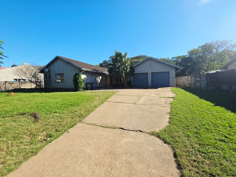 Front view of a single-story house featuring a double garage, concrete driveway, and a large front lawn with perimeter boundary walling.