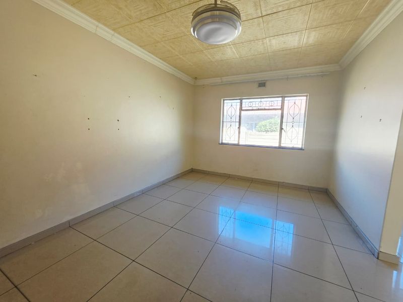 An empty bedroom featuring tiled flooring, a textured ceiling, and a window with security bars, requiring minor cosmetic wall repairs.