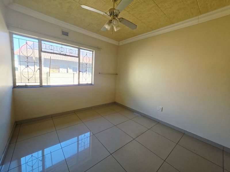 A vacant bedroom featuring tiled flooring, a ceiling fan, and security bars on the window.