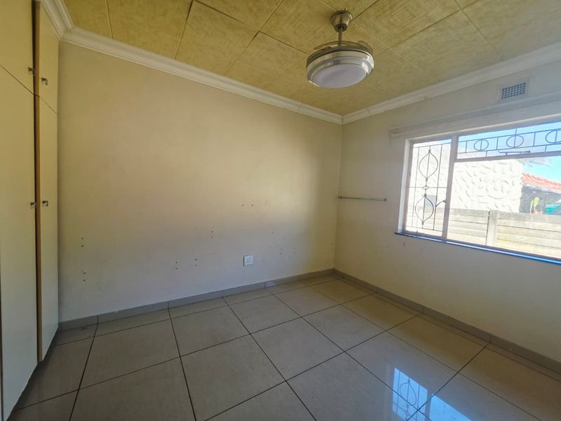 An empty bedroom featuring tiled flooring, built-in cupboards, and a ceiling fan, requiring minor cosmetic updates to the walls and ceiling.