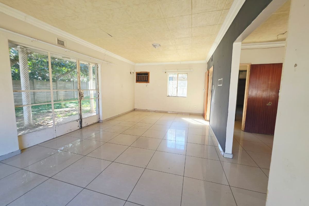 Spacious, empty living area featuring tiled floors, decorative ceiling tiles, and large sliding glass doors providing access to the garden.