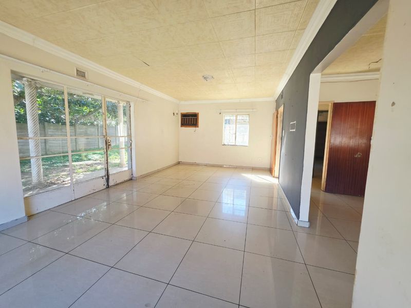 Spacious, empty living area featuring tiled floors, decorative ceiling tiles, and large sliding glass doors providing access to the garden.