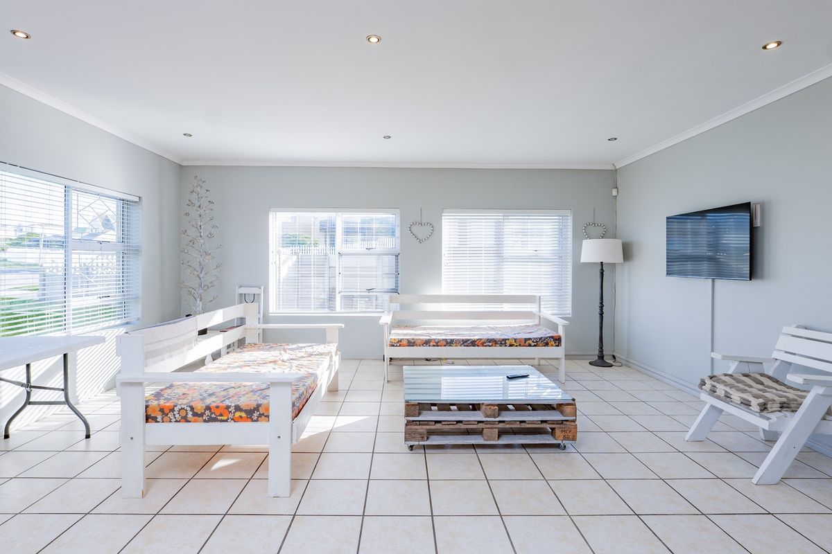 A bright and spacious living room featuring neutral tiled flooring, recessed downlighting, and multiple windows fitted with venetian blinds.