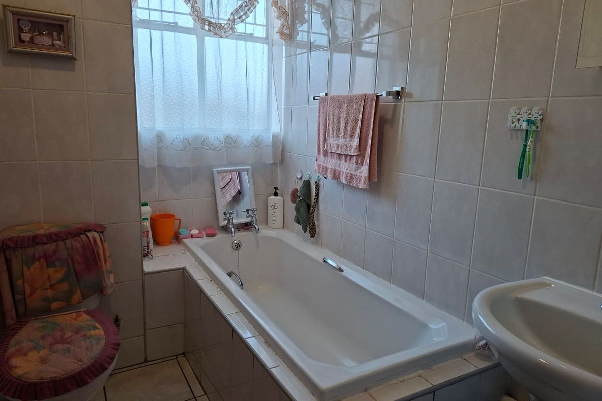 A functional bathroom featuring a built-in bathtub, wall-mounted basin, and full-height wall tiling.