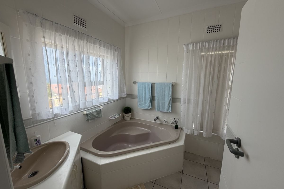 A functional bathroom featuring a corner bathtub, vanity basin, and tiled finishes, offering a dated aesthetic ready for modernization.